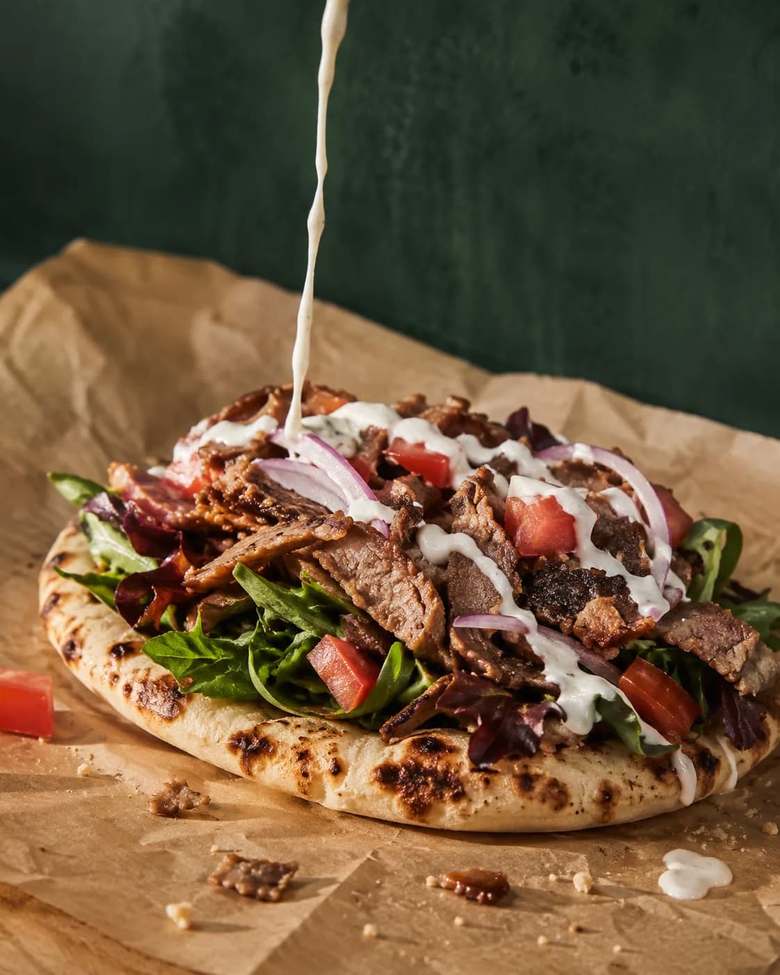 Garlic sauce pouring over an open pita piled with beef shawarma